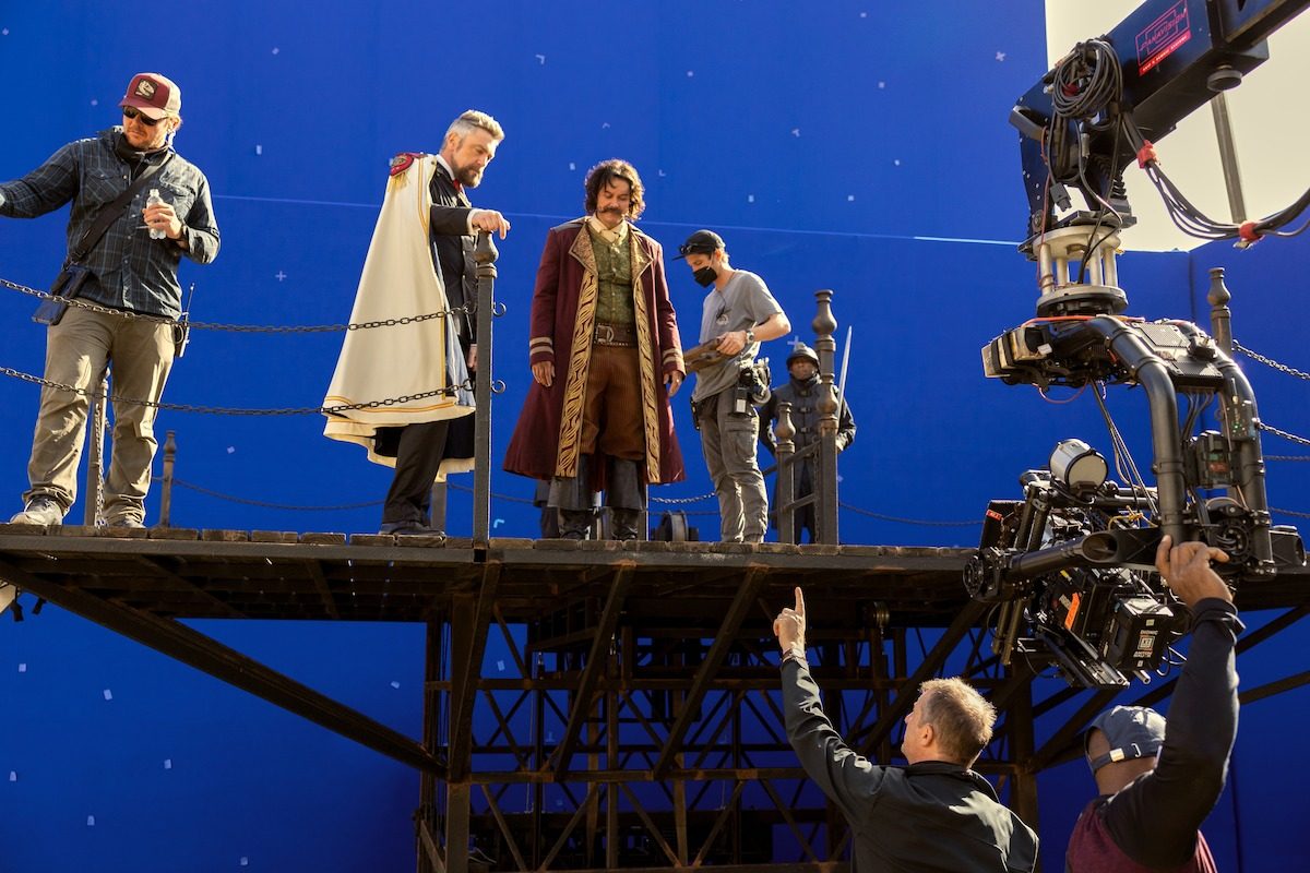 Crew members on a raised platform set piece against a blue screen, with a camera crane arm swinging into position beside them